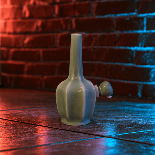 Glossy Green Flat-Sided Celadon Ceramic BongA glossy pale green ceramic bottle or vase with a long narrow neck and a small protruding bulb-like detail on the side, standing on a dark wooden surface against a red brick wall with blue and red lighting.