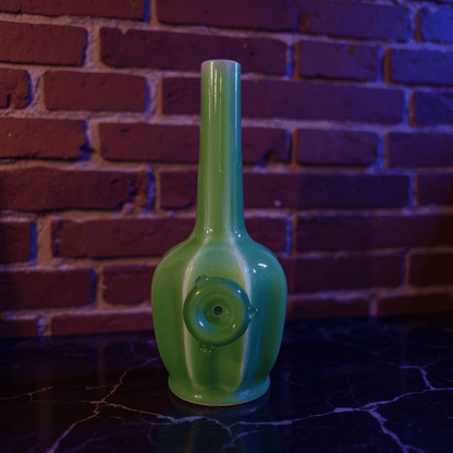 Glossy Green Flat - Sided Celadon Porcelain BongGreen ceramic smoking pipe on a dark surface with a brick wall background