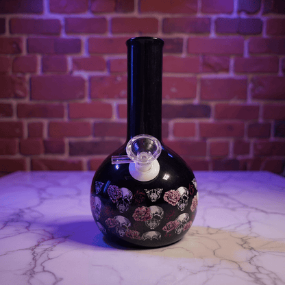 Gothic Skull Rose Ceramic Bong – Black ceramic bong with colorful designs on a marble surface against a brick wall.
