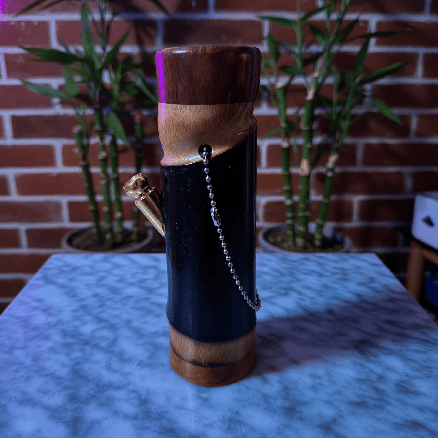 Handcrafted Bamboo Bong – Eco - Friendly Water Pipe with Natural AromaWooden bamboo bong with a chain on a marble surface with plants in the background