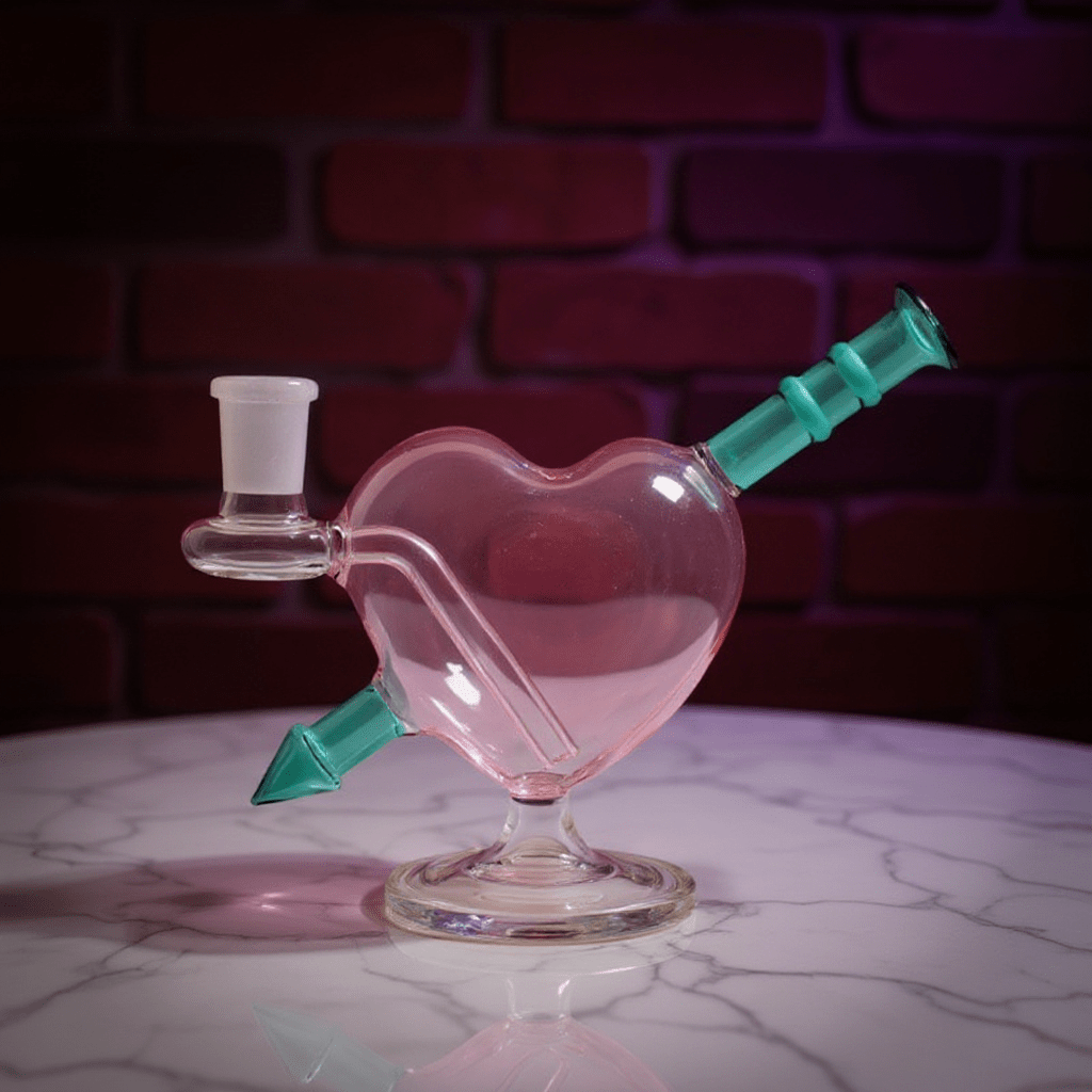 Heartpiercer Water Pipe – Mint Arrow EditionHeart - shaped glass pipe with teal accents on a marble surface against a brick wall background