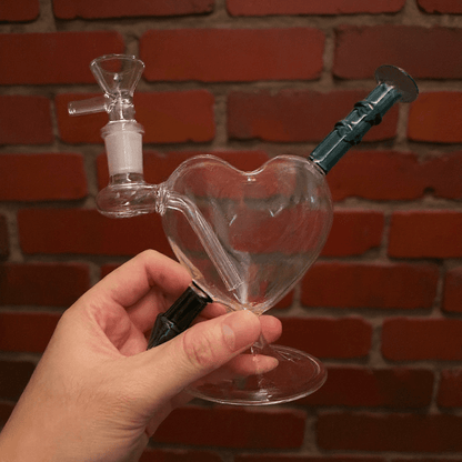 Heartpiercer Water Pipe – Mint Arrow EditionHeart - shaped glass pipe held by a hand against a brick wall background