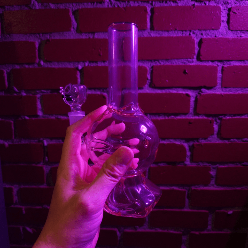 Hello Glow Mini Bong – Cute Style with Crystal Glass. Clear pink hello kitty glass water pipe held against a brick wall