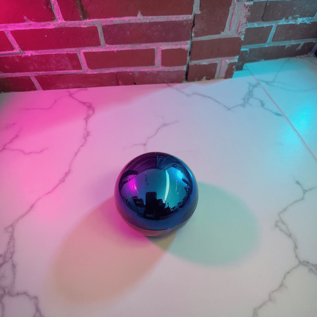Holographic Ball Herb Grinder Multicolored reflective tobacco grinder on a marble surface with a brick wall background