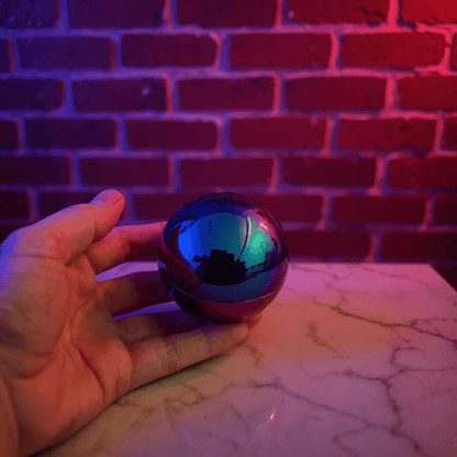 Holographic Ball Herb Grinder Hand holding a reflective tobacco grinder against a brick wall with red lighting