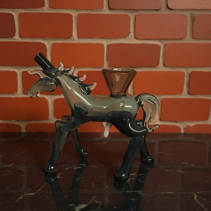 Horse Glass Hand Pipe - Glass horse pipe with amber - colored glass on a reflective surface in front of a brick wall.