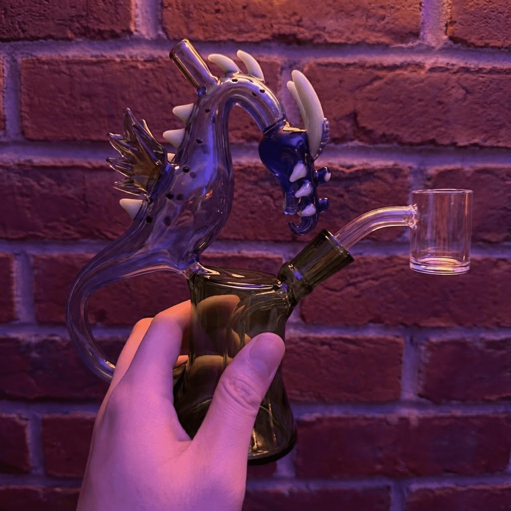 House of Dragon Glass Bong – RPG & Anime Style Water PipeGlass smoking bong with dragon design held against a brick wall.