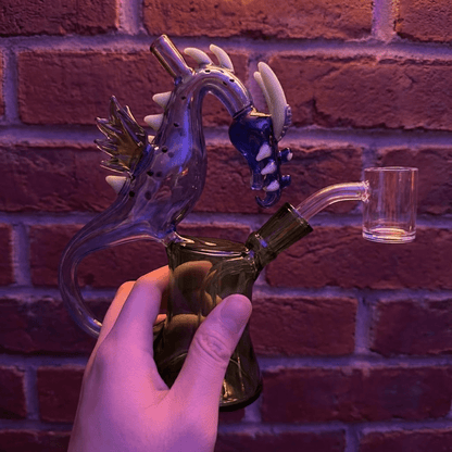 House of Dragon Glass Bong – RPG & Anime Style Water PipeGlass smoking bong with dragon design held against a brick wall.