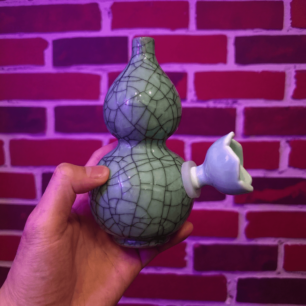 Ice - Crack Blue Celadon Gourd Porcelain BongHand holding a ceramic gourd bong against a brick wall background