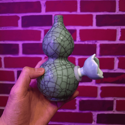 Ice - Crack Blue Celadon Gourd Porcelain BongHand holding a ceramic gourd bong against a brick wall background