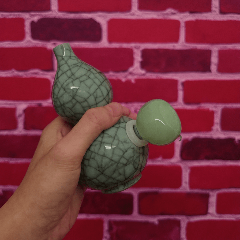 Ice - Crack Blue Celadon Gourd Porcelain BongHand holding a green ceramic bong against a red brick wall