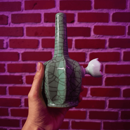 Ice - Crack Light Blue Celadon Flat - Sided Porcelain BongHand holding a ceramic bong with a textured design against a brick wall