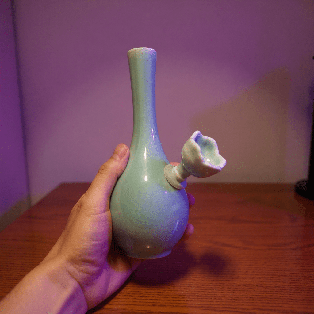 Light Green Slim Neck Celadon Porcelain BongHand holding a light green ceramic bong with a unique design on a wooden surface.
