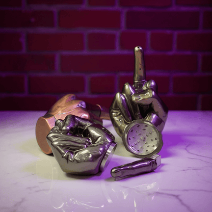 Middle Finger Grinder & Pipe Combo – Heavy Duty 2 - in - 1 SystemMetallic hand - shaped grinders on a marble surface with a brick wall background