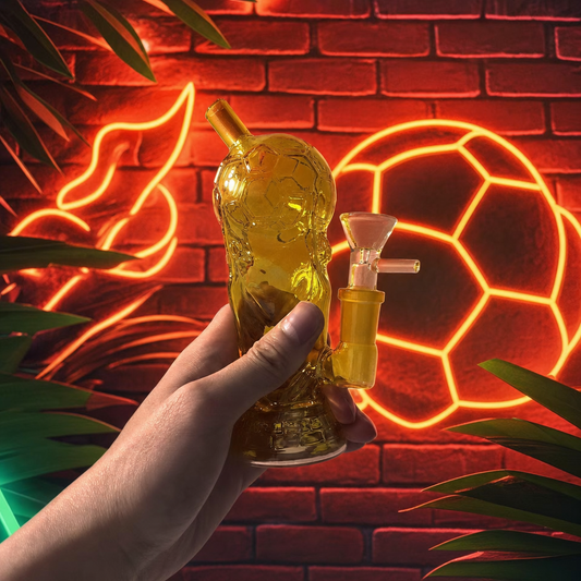 Hand holding a glass smoking device with neon lights and brick wall in the background