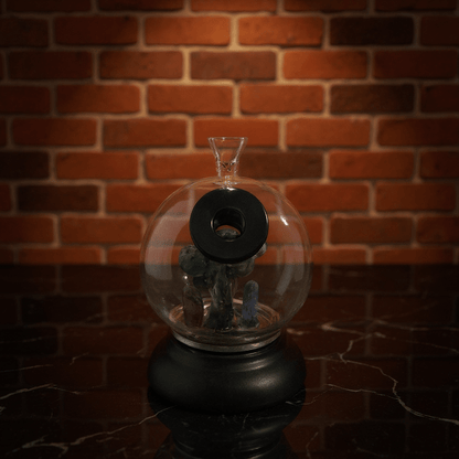 Mushroom Globe Bong - Glass bong with miniature scene on a black stand against a brick wall.