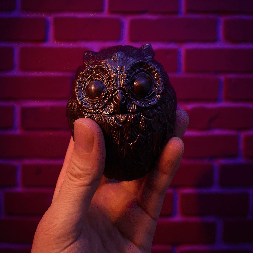 Hand holding a decorative owl grinder against a brick wall with purple lighting
