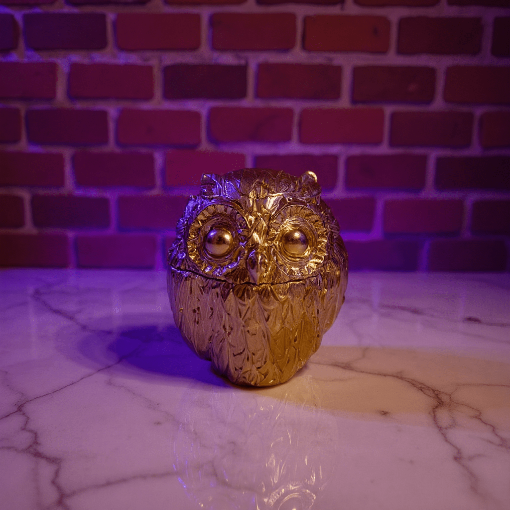 Gold owl - shaped decorative grinder on a marble surface with a brick wall background