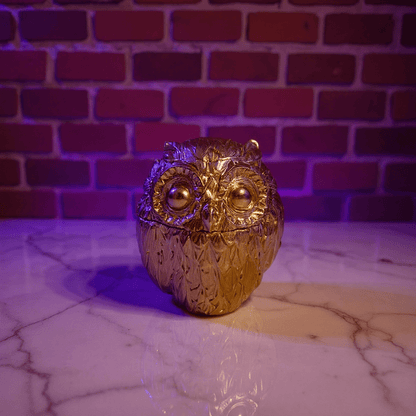 Gold owl - shaped decorative grinder on a marble surface with a brick wall background