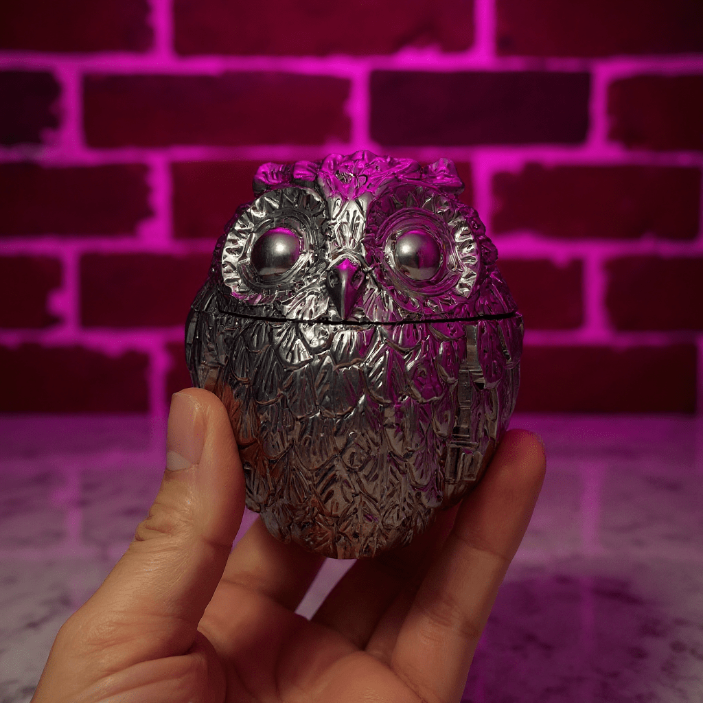 Silver owl - shaped grinder held in front of a pink brick wall