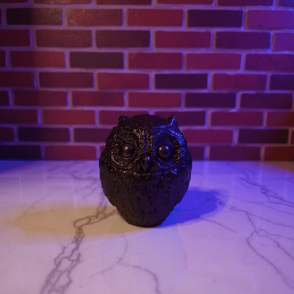 Decorative owl grinder on a marble surface with a brick wall background