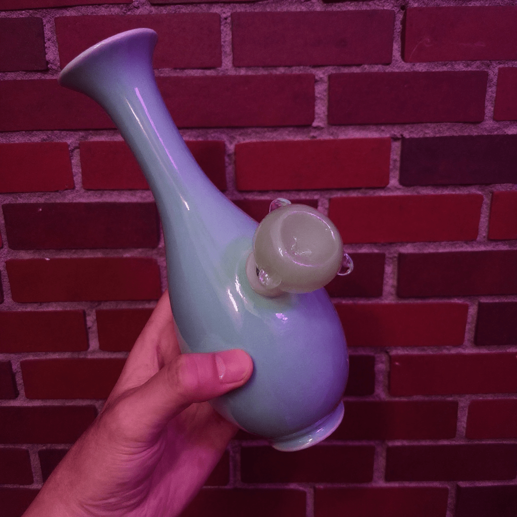 Pale Blue Flared Top Celadon Porcelain BongHand holding a light blue and green ceramic pipe against a red brick wall.
