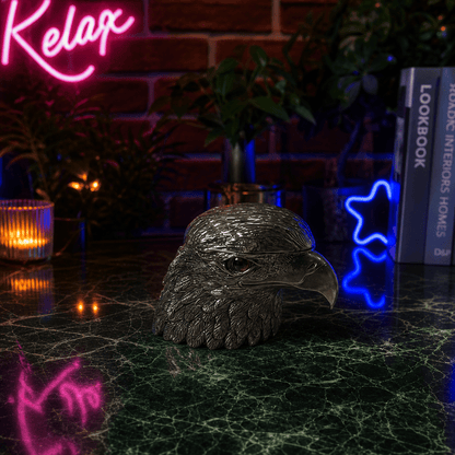 Patriot Eagle Head Metal Grinder – Brass, Bronze & Black FinishMetallic eagle head sculpture on a dark surface with neon signs and books in the background.