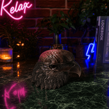Patriot Eagle Head Metal Grinder – Brass, Bronze & Black FinishDecorative eagle head sculpture on a dark surface with neon signs and books in the background.