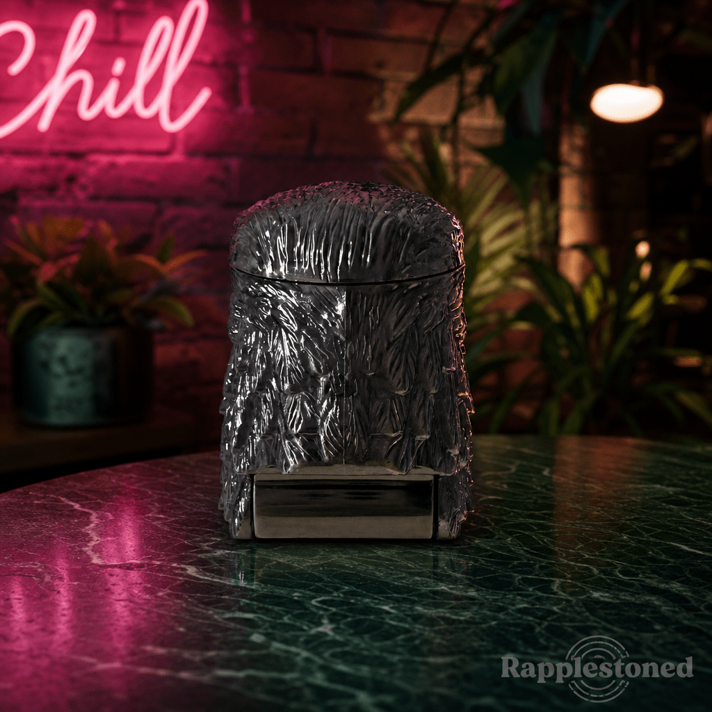 Patriot Eagle Head Metal Grinder – Brass, Bronze & Black FinishMetallic textured grinder on a reflective surface with a neon 'Chill' sign in the background