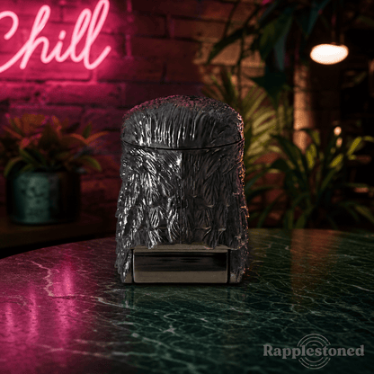 Patriot Eagle Head Metal Grinder – Brass, Bronze & Black FinishMetallic textured grinder on a reflective surface with a neon 'Chill' sign in the background