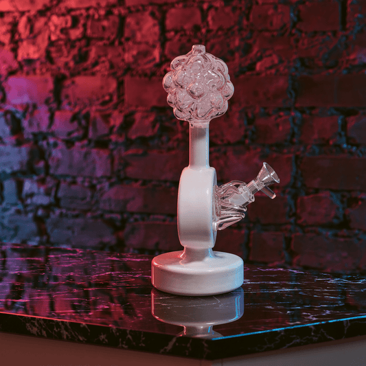 Plumbus-Inspired Sculptural BongA hand holds a decorative cylindrical bamboo box with black branch-like engravings, a gold frog clasp, and a beaded strap, set against a dark brick wall with purple ambient lighting and plants.