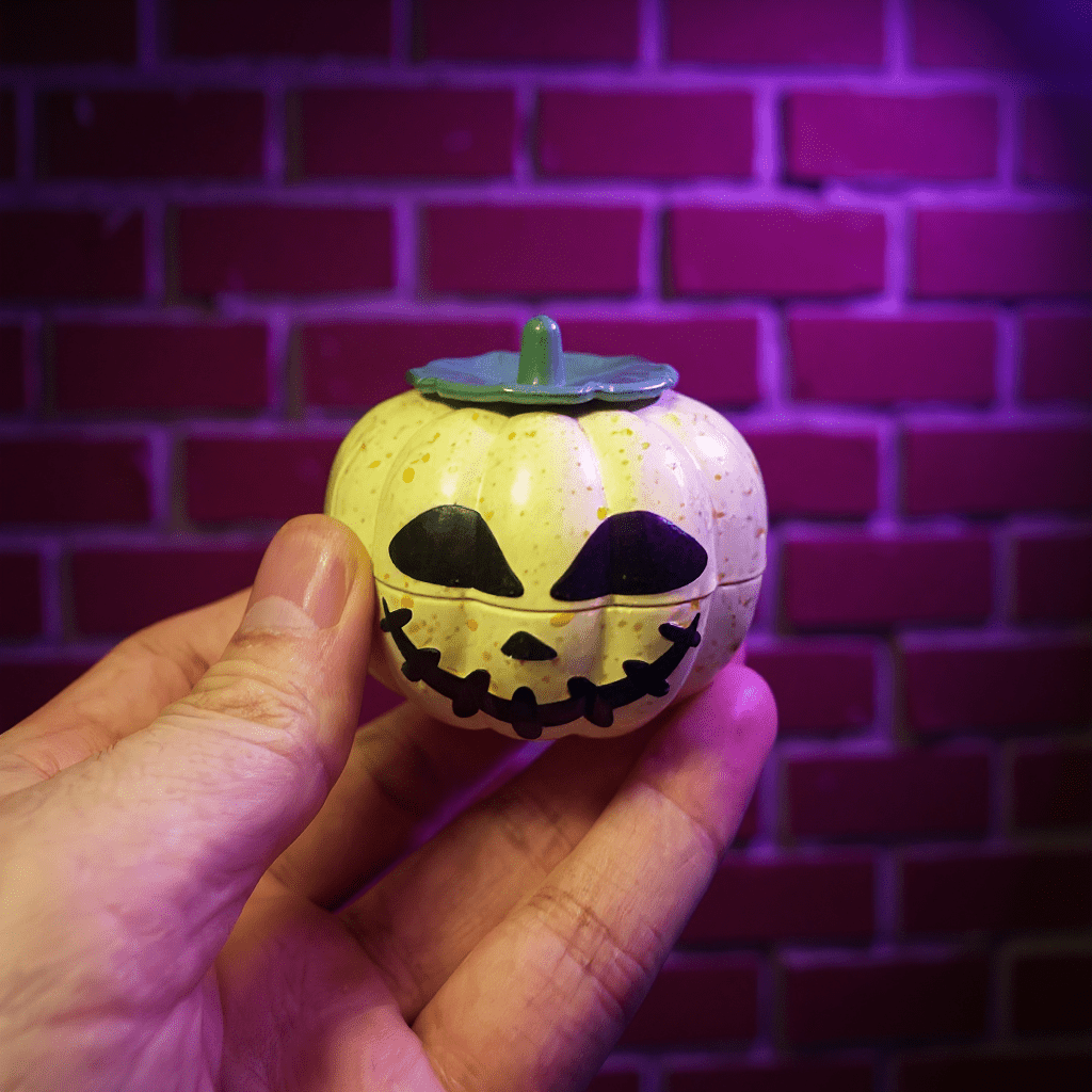 Pumpkin Herb Grinder – 3 - Piece GrinderHand holding a small pumpkin - shaped grinder with a face