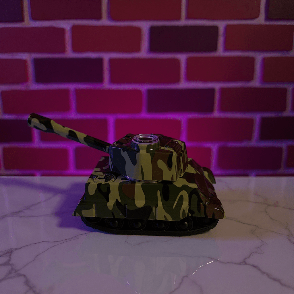 Toy tank grinder with camouflage design on a reflective surface against a brick wall background