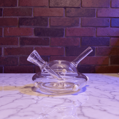 UFO Mini Glass Bong – Water Pipe in 3 Colorspink glass smoking bong on a marble surface with a brick wall background